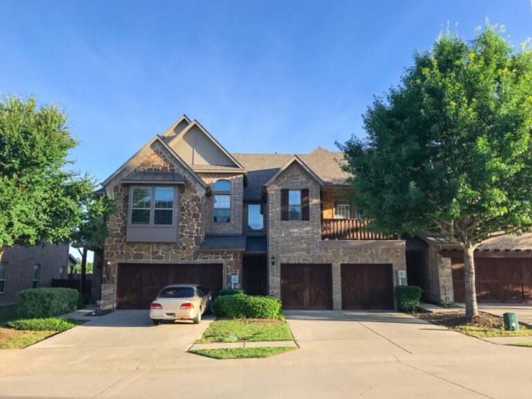 a brick two story home with multiple garage and a tree on the side