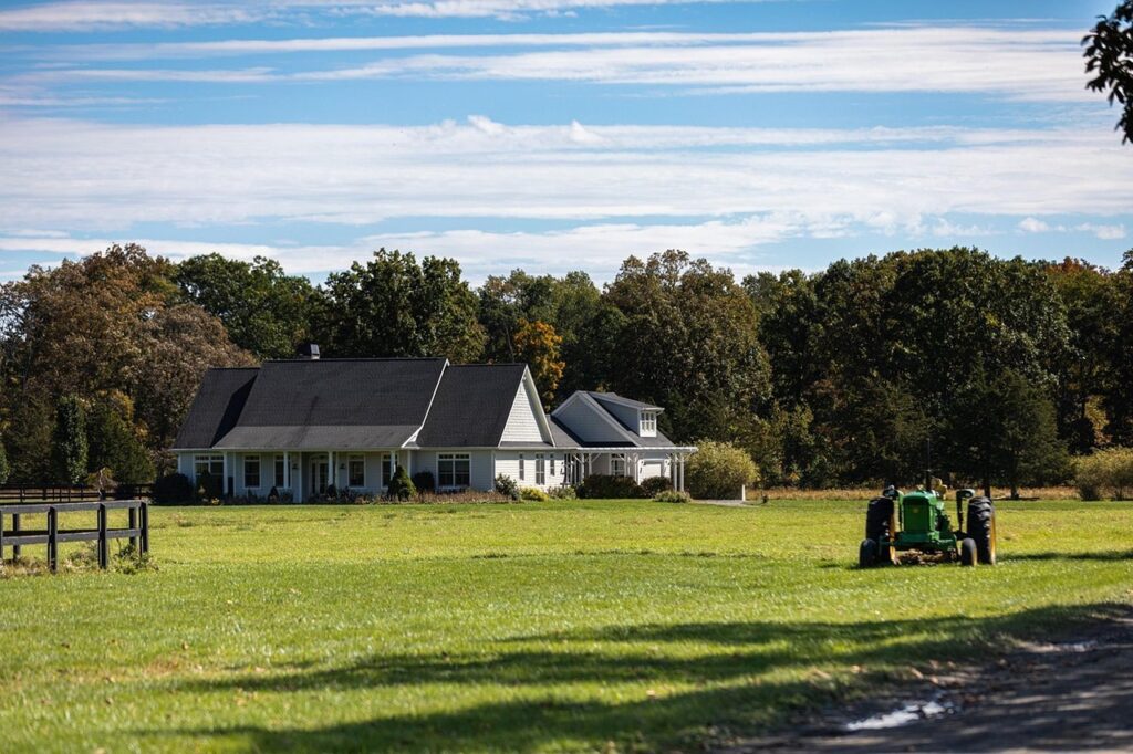 a house surrounded by trees and grassy field and a tractor in the middle of the field