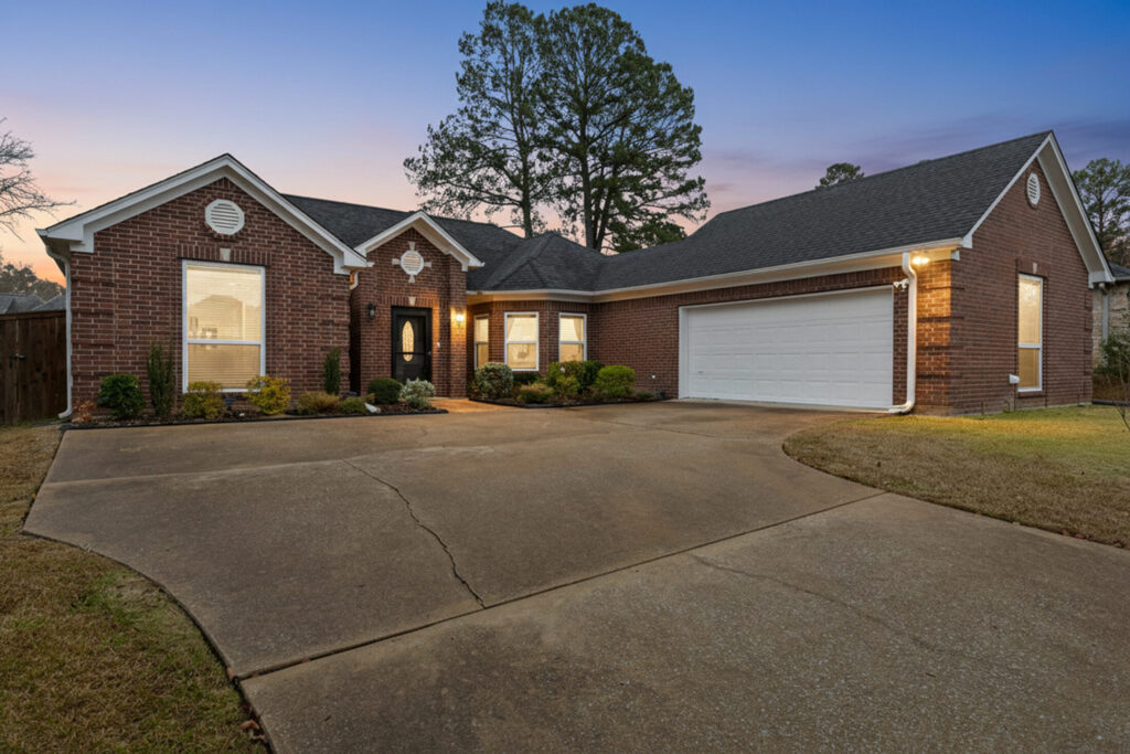 a single-story red brick house with an attached two-car garage and a curved concrete driveway