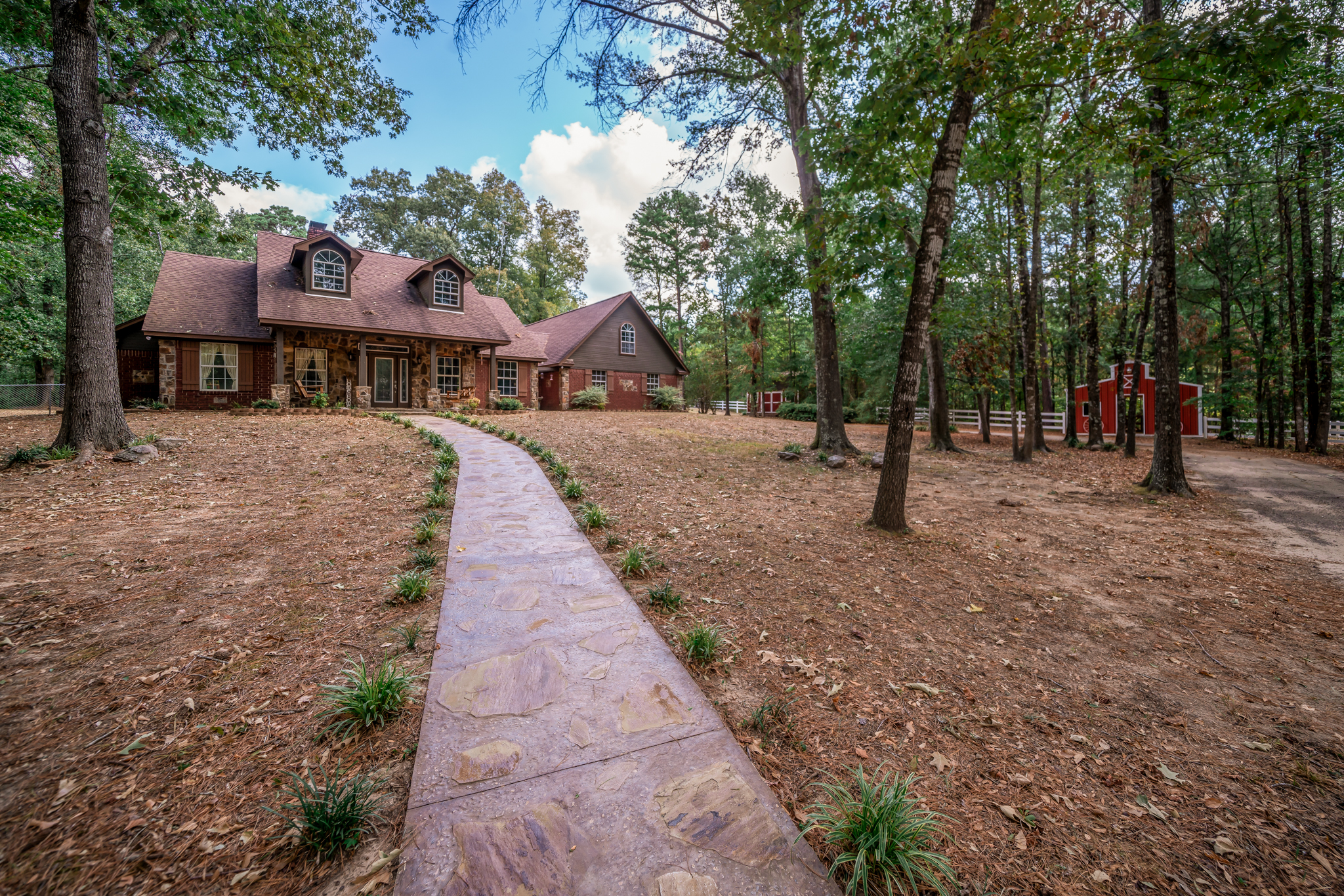 a stone and wood-sided house located on a large, wooded property