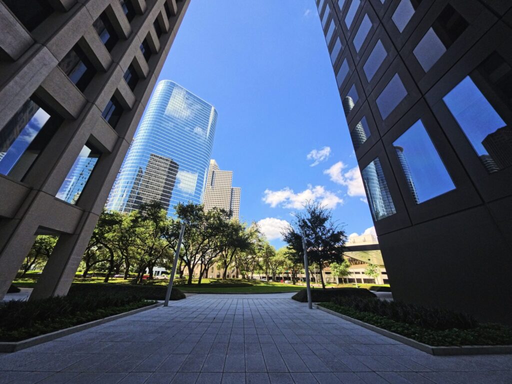 A low-angle shot looking up between tall modern office skyscrapers framing a clear blue sky