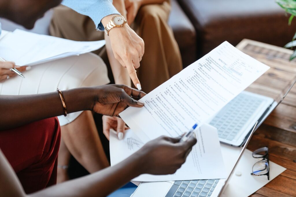 Close-up of colleagues reviewing printed documents together on a table next to a laptop and eyeglasses